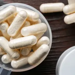 Kapsułki z naturalną glukozaminą w miarce i obok otwartego pojemnika.