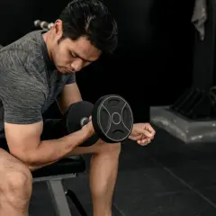 Mężczyzna ćwiczy biceps z hantlem. Energia do treningu pochodzi z glikogenu, który jest zapasem cukru w mięśniach.